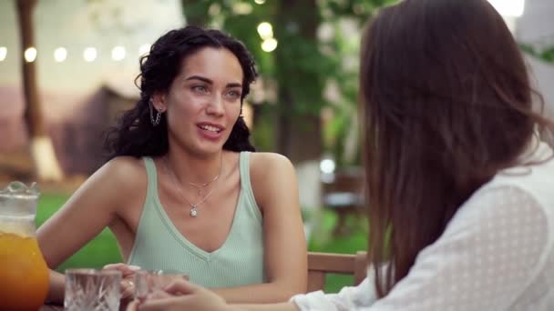 Ludzie, koncepcja komunikacji i przyjaźni - uśmiechnięte młode kobiety pijące sok pomarańczowy i rozmawiające w kawiarni — Wideo stockowe
