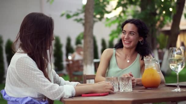 Menschen, Kommunikations- und Freundschaftskonzept - lächelnde junge Frauen, die trinken, im Outdoor-Café reden, brünett gute Nachrichten oder Klatsch teilen — Stockvideo