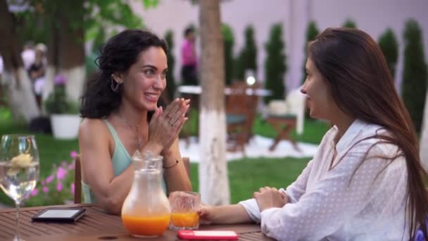 Mensen, communicatie en vriendschap concept - glimlachende jonge vrouwen praten in outdoor cafe, brunette delen van goed nieuws, gebaren, klappen — Stockvideo