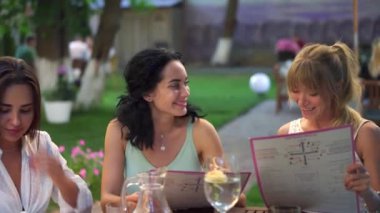 Üç güzel kız arkadaşın portresi menü okuyor ve halka açık parktaki kafede birlikte eğleniyorlar.