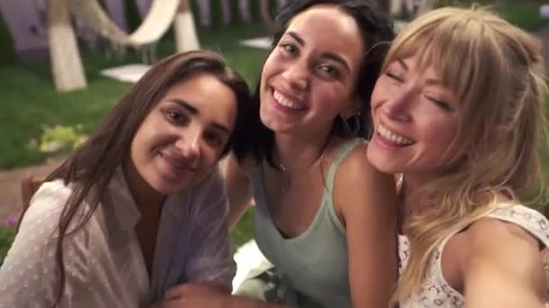 Tres mujeres alegres se conocieron en la cafetería de la veranda al aire libre tomando foto o video selfie en el teléfono inteligente, divirtiéndose, bebiendo — Vídeo de stock