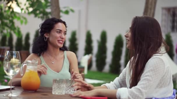 People, communication and friendship concept - two women drinking orange juice, talking at outdoor cafe, laughing — Stock Video