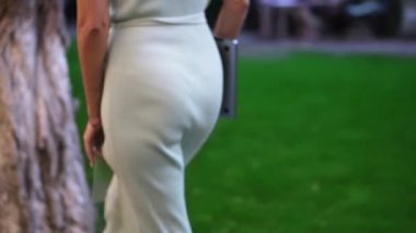 Elbiseli bir kadın parkta ağacın altında oturmaya gelir, dizüstü bilgisayarı açar, dizlerinin üstüne koyar ve yazmaya başlar.