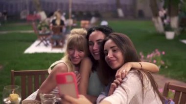 Veranda kafesinde sohbet eden kaygısız kadınlar akıllı telefondan selfie ya da video çekiyorlar.