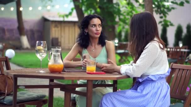 Mensen, communicatie en vriendschap concept - glimlachende jonge vrouwen praten in outdoor cafe, het delen van goed nieuws, gebaren — Stockvideo