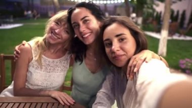 Veranda kafeteryasında tanışan üç çekici kadın akıllı telefondan selfie ya da video çekiyor.