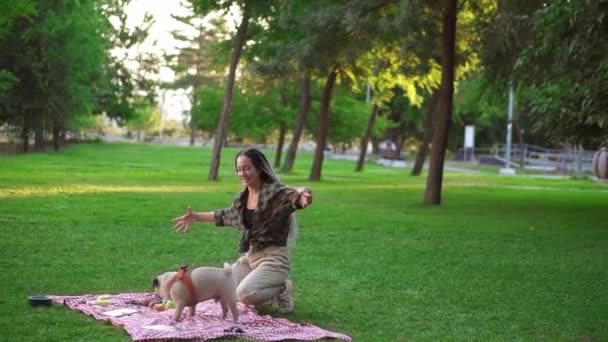 Vrouw met dreadlocks spelen met haar hond op gras, picknick buiten in het groene park alleen — Stockvideo