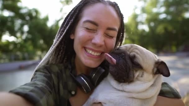 Νεαρή κοπέλα κρατάει το σκύλο της. Ένα χαριτωμένο μπεζ κουτάβι προσπαθεί να γλείψει το πρόσωπο. Μια γυναίκα κρατάει κάμερα. — Αρχείο Βίντεο