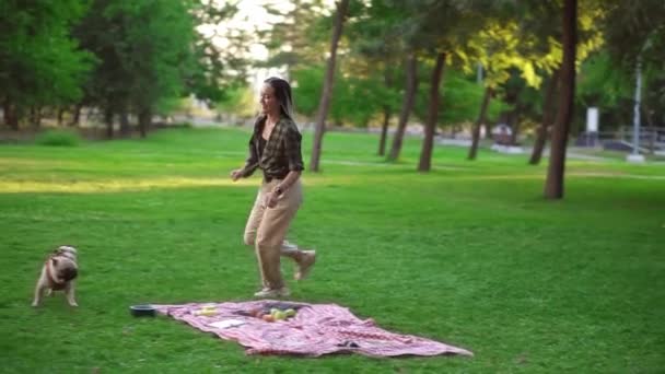 Feliz, joven mujer divirtiéndose con su perro al aire libre - corriendo, persiguiéndolo a cuadros con picnic en la hierba — Vídeo de stock