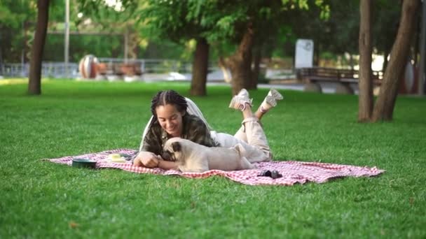 Woman with dreadlocks playing with her dog on grass, laying on plaid - tricking him with a little snack — Stock Video