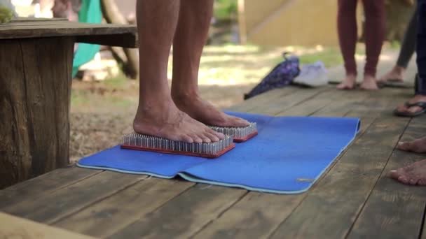 Piedi maschili passo su una tavola da yoga in legno con un sacco di chiodi metallici spilli intorno a diverse persone irriconoscibili — Video Stock