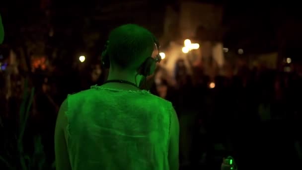 Amigos están bailando por la noche teniendo una fiesta al aire libre mientras DJ está trabajando con el equipo, material de archivo de la parte posterior — Vídeos de Stock