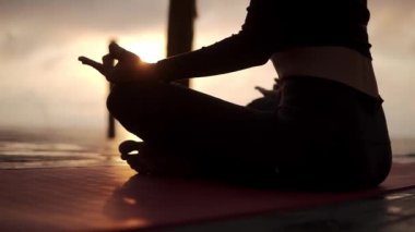 Nilüfer çiçeğinin önünde oturmuş meditasyon yapan, dizlerinin üzerinde parlayan, tanınmayan bir Yogi kızı silueti.