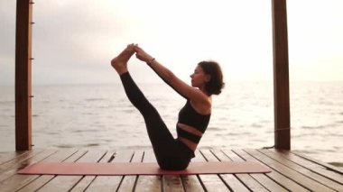 Deniz rıhtımında yoga yapan kadın Ubhaya Padangusthasana 'yı canlandırıyor.