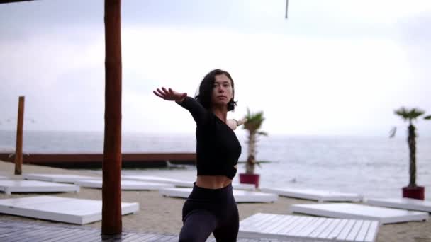 Concentrated woman is doing yoga on mat on the beach, the girl performs yoga stands and elements - warrior — Stock Video