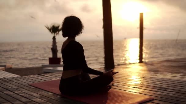 Дівчинка Йогі сидить у позі лотоса перед морем влітку на заході сонця і медитує. — стокове відео