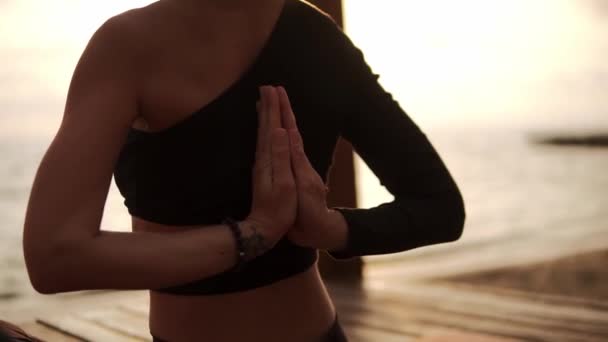 Žena cvičí jógu a protahuje páteř a ruce sedí na podložce na mořském molu - spojuje ruce za zády — Stock video