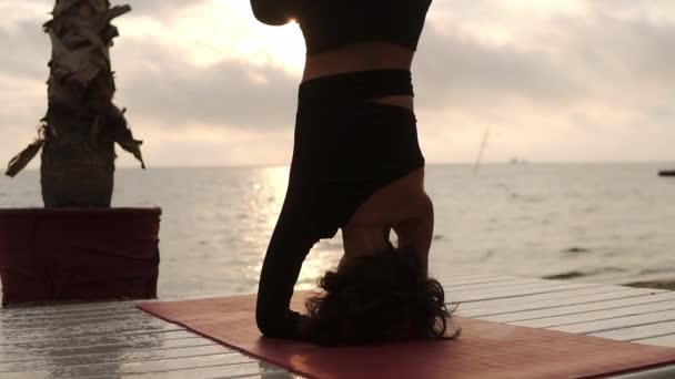Kobieta stojąca na głowie w jodze poza salamba shirshasana na świeżym powietrzu, praktykująca jogę asana na letnim tarasie przed morzem — Wideo stockowe