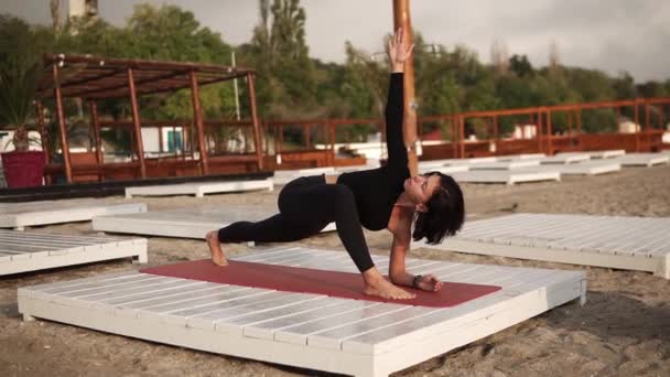 Mulher branca praticando ioga no tapete na praia realizando ioga ou alongamento pernas, realizando pose de ângulo lateral estendido — Vídeo de Stock