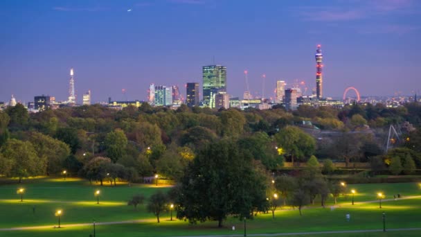黄昏时分, 从普里姆罗斯山公园欣赏伦敦全景。前景是公园的树木和灯光, 背景是伦敦的天际线. — 图库视频影像