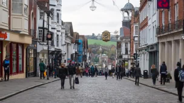 Zona comercial peatonal bulliciosa de High Street con decoración navideña festiva y con el hito local del reloj de la ciudad del guildhall sobre la calle. Guildford, Surrey, Reino Unido . — Vídeo de stock