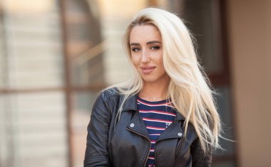 Genç sarışın kızın güzel yakın çekim portre giyen siyah ceket açık havada gözler. Uzun dalgalı saç güzel kadın var. Kadın kentsel arka planda.