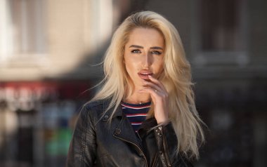 Genç sarışın kızın güzel yakın çekim portre giyen siyah ceket açık havada gözler. Uzun dalgalı saç güzel kadın var. Kadın kentsel arka planda.