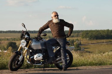 Motorcu ihtiyar bir deri ceket ve onun motosiklet üzerinde oturan güneş gözlüğü takmış.