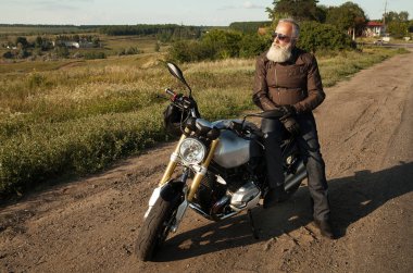 Motorcu ihtiyar bir deri ceket ve onun motosiklet üzerinde oturan güneş gözlüğü takmış.