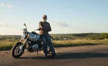 Motorcu ihtiyar bir deri ceket ve onun motosiklet üzerinde oturan güneş gözlüğü takmış.