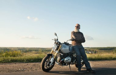 Motorcu ihtiyar bir deri ceket ve onun motosiklet üzerinde oturan güneş gözlüğü takmış.