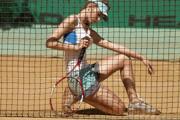 試合後テニスコートに座って残りの部分を持っている帽子を被った若い美しい女性のテニス選手 — ストック写真