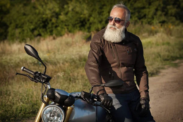 Old Biker man wearing a leather jacket and sunglasses sitting on his motorcycle.