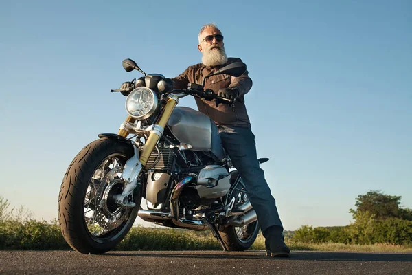 Old Biker man wearing a leather jacket and sunglasses sitting on his motorcycle.