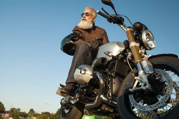 Old Biker man wearing a leather jacket and sunglasses sitting on his motorcycle.