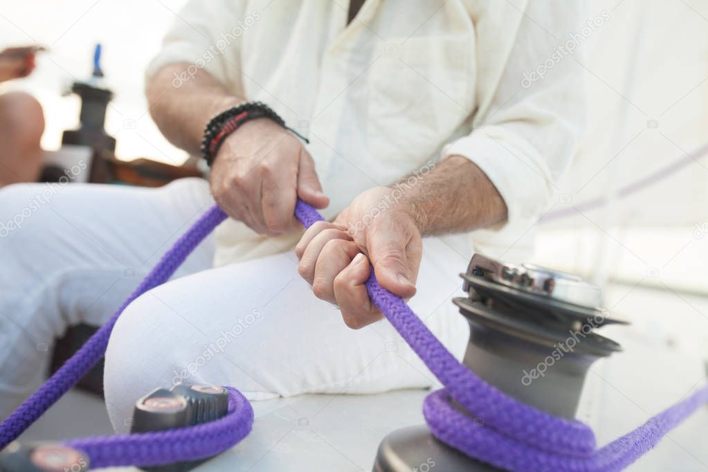 Close-up: an elderly man unravels a rope on a sailing boat. It is never too late to master skills of sailing. Concept: active elderly people.