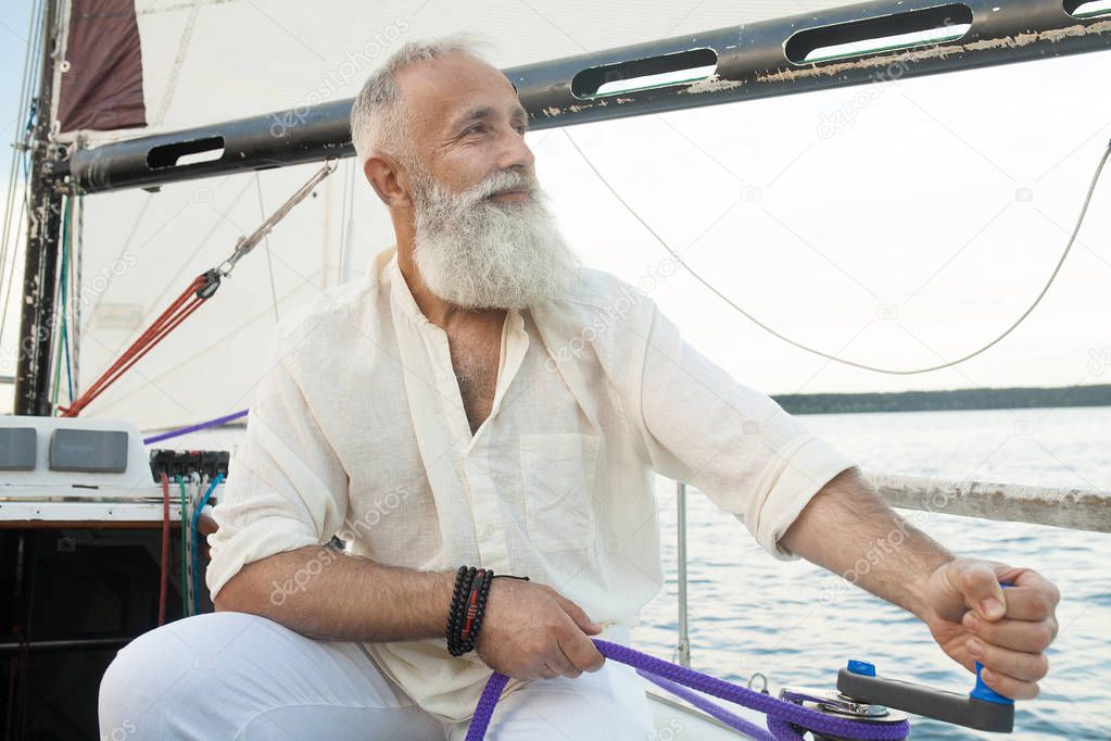 Close-up: an elderly man unravels a rope on a sailing boat. It is never too late to master skills of sailing. Concept: active elderly people.