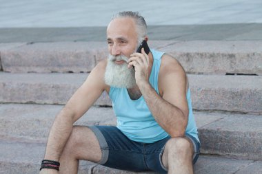 Merdivenlerde oturan ve telefonda konuşurken komuta sizde. Mutlu sakallı adam.