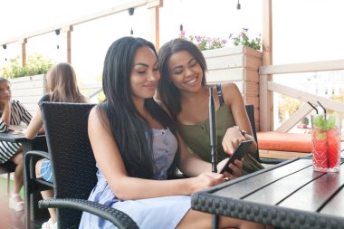 Çok ırklı kadınlar olumlu haber üstünde hareket eden telefon ile bildirimi okuyun, boş zamanlarını Teras Cafe, birbirinize sarılın, mutlu ifadeler. İki diveristy kadın bir şey Internet seçmek