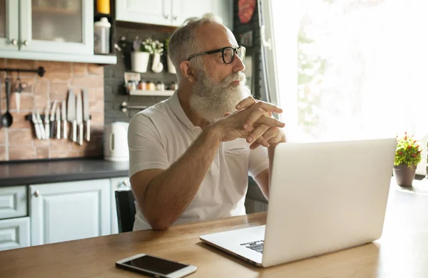 Bearded Senior man in living-room using laptop computer
