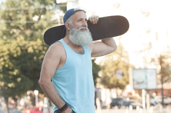 Happy bearded old man. The concept of life satisfaction. Portrait of a positive gray-haired man with a skateboard. Winner concept.