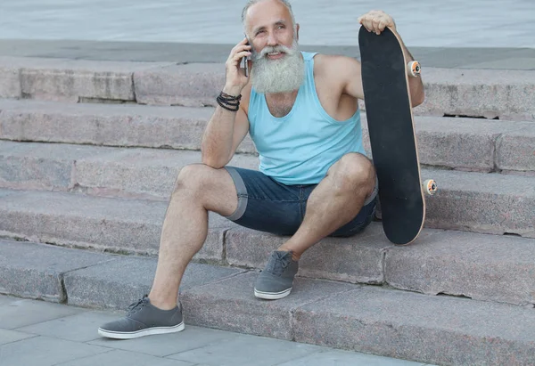 trendy old bearded man  with skateboard in town, relaxing on stairs