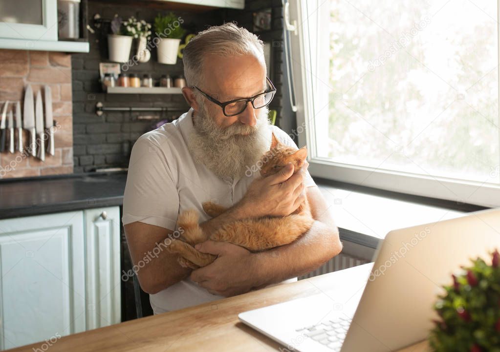 Elderly man with his cat working on laptop, smiling, looking at screen.