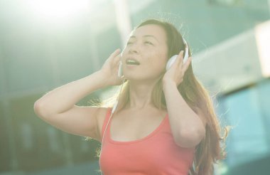 Asyalı kadın mutlu gülümseme ve telefon dinlemek müzik yaşayan kullanın