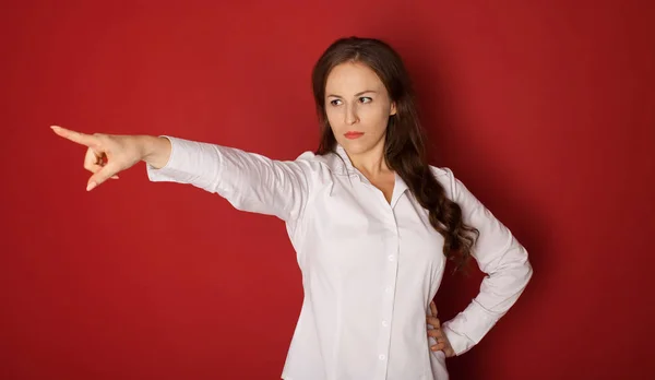 portrait of angry woman in formal wear pointing finger at something. isolated on red background