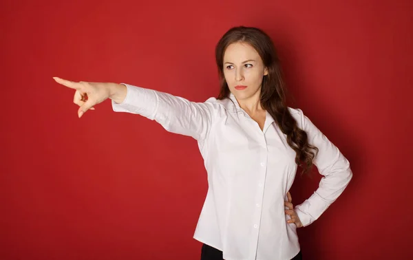 portrait of angry woman in formal wear pointing finger at something. isolated on red background