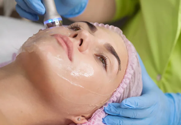 Beautiful woman getting radio frequency lifting on her face. Professional beautician doing anti-wrinkle facial treatment. Concept of skin care and correction of skin texture.