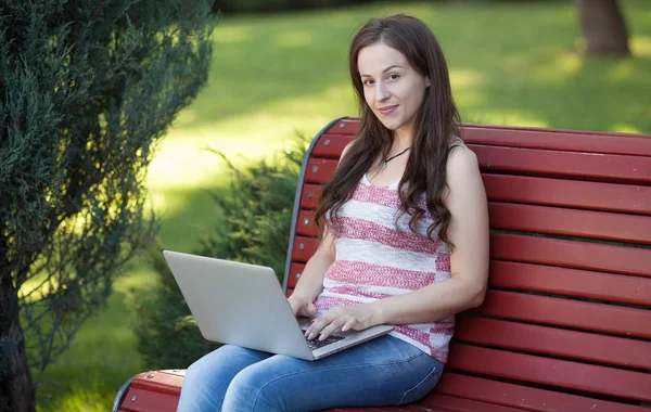 美しい白人女性は に接続して ラップトップを持つ都市公園でベンチに座っています 起業家は 都市の背景をぼかしながら屋外ポータブル コンピューターに取り組んでいます — ストック写真