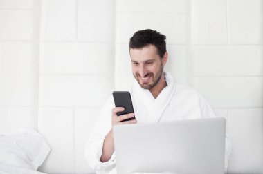 Telefonunu yatak kullanan genç adam.