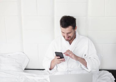 Telefonunu yatak kullanan genç adam.